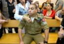 A man in military uniform sits on a wooden bench in a courtroom and is comforted by a woman.