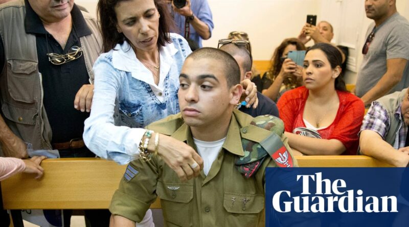 A man in military uniform sits on a wooden bench in a courtroom and is comforted by a woman.