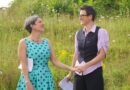 The couple holding hands in a field, while also holding printouts of their vows