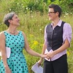 The couple holding hands in a field, while also holding printouts of their vows