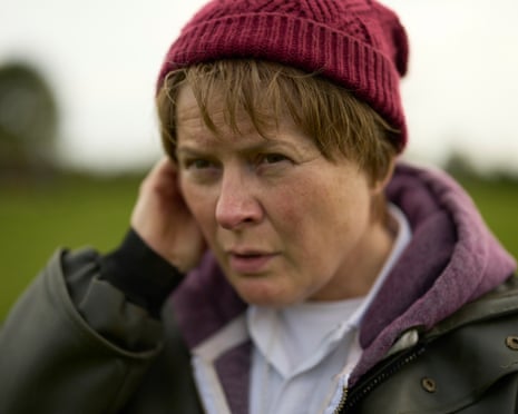 Monica Dolan, as Catherine Corless, touches her ear with a concerned expression outdoors