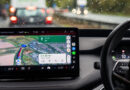An in-car infotainment display shows a Google Maps navigation route while the vehicle is being driven in rainy traffic.